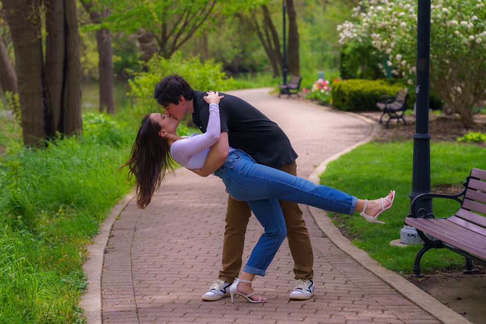 A couple playfully poses together on a brick pathway surrounded by greenery.