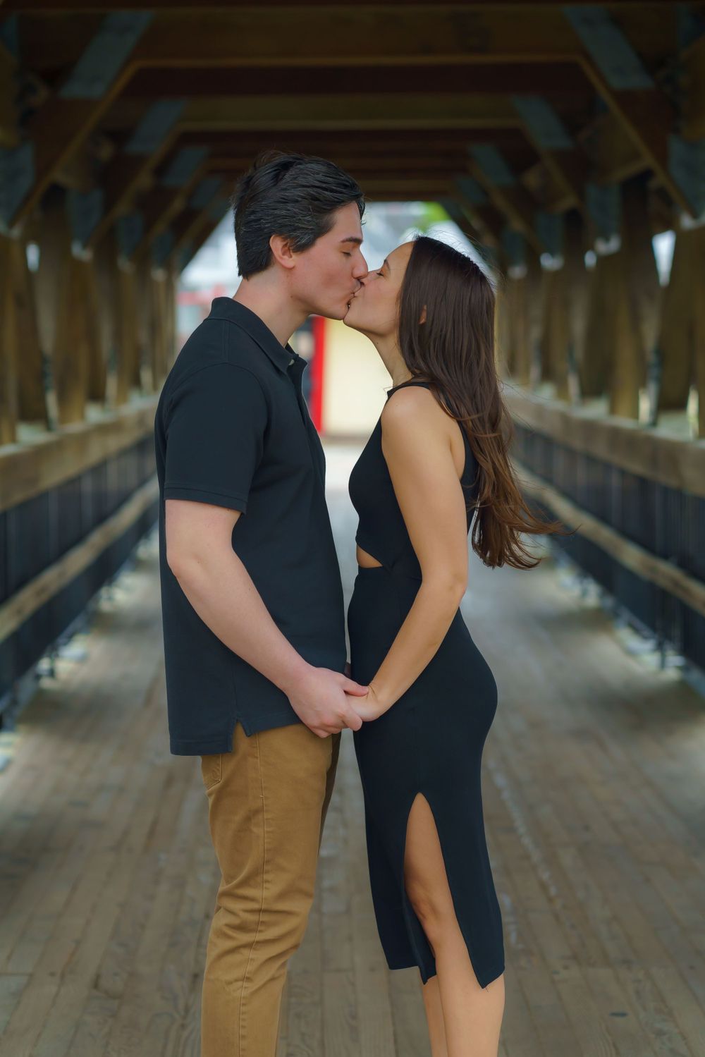 A romantic couple embraces in a covered wooden bridge with natural lighting.