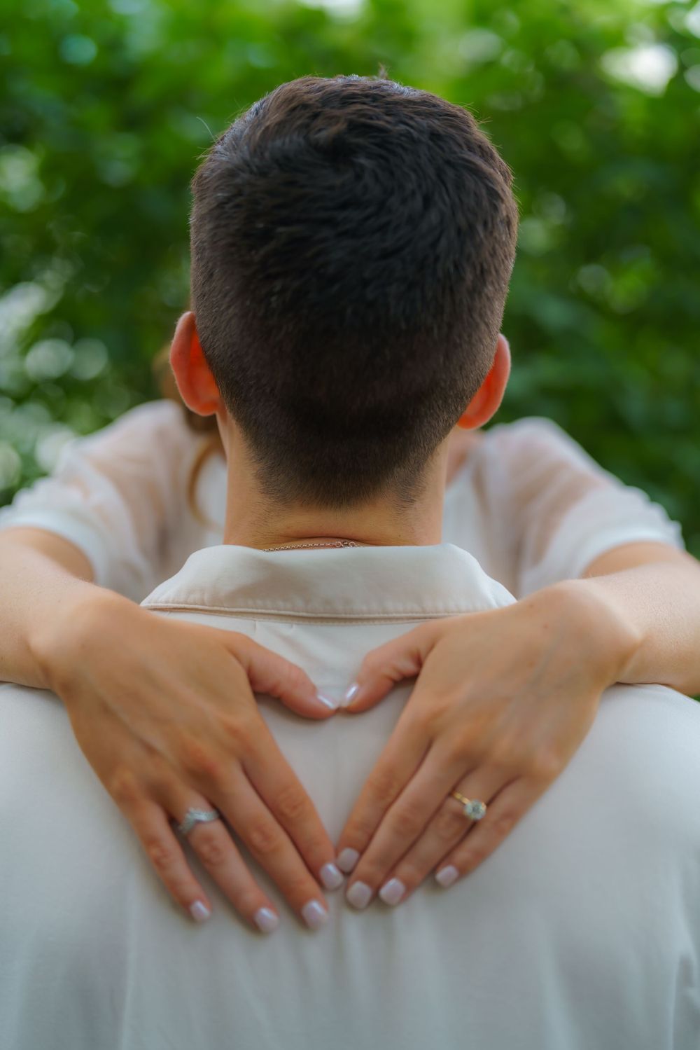 Close-up of hands embracing from behind, showing an engagement ring.