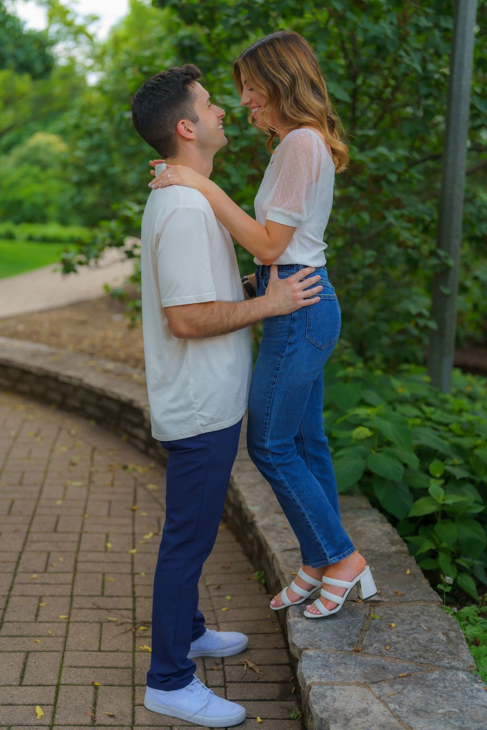 A couple shares tender moments on a stone wall in a garden setting.