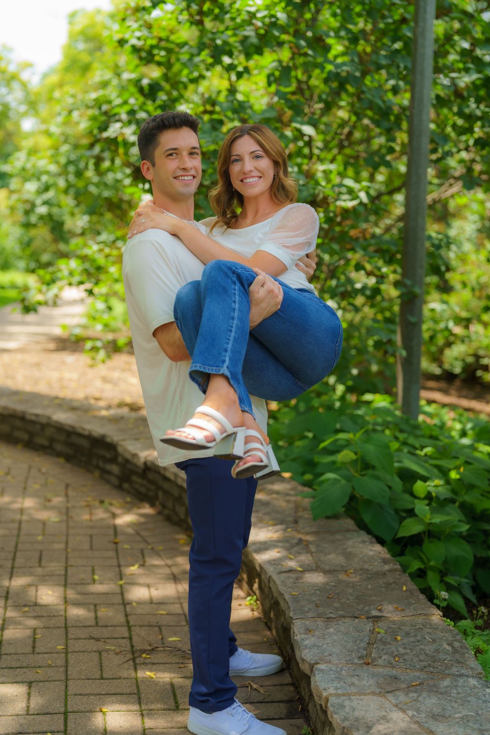 A couple plays and laughs together on a brick garden path.