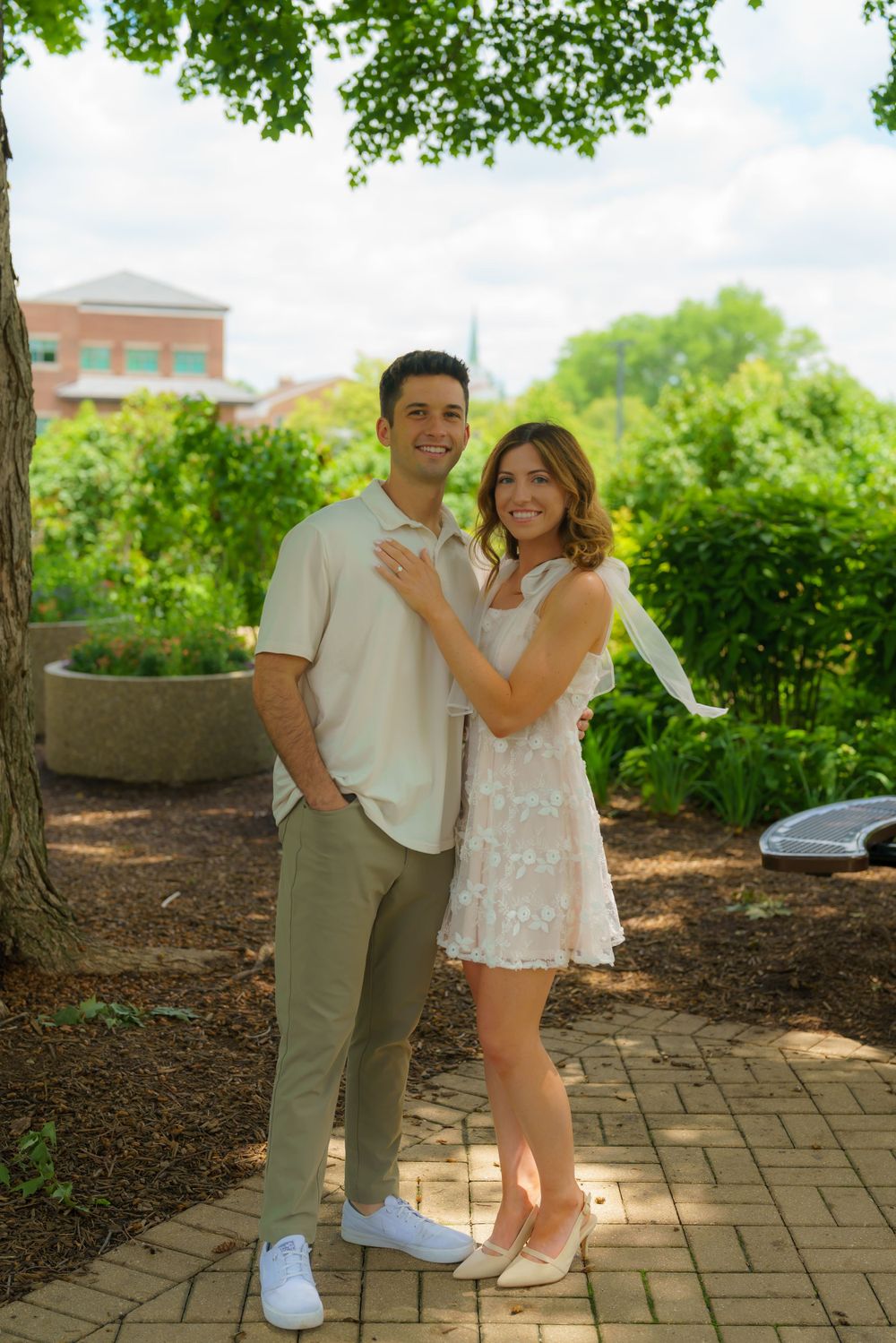 Playful couple embraces on a brick pathway surrounded by landscaped garden grounds.