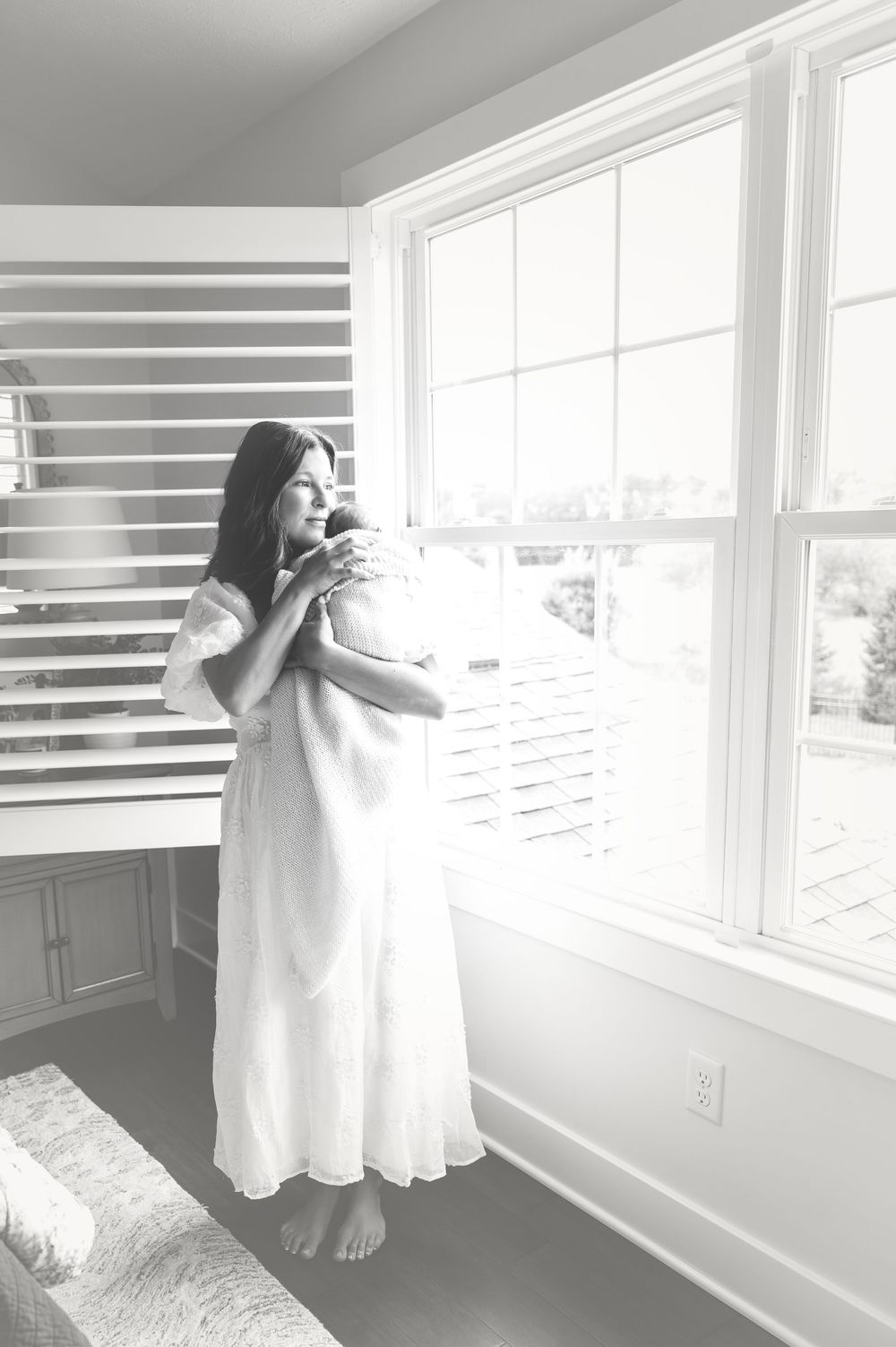 Delicate silhouette of a figure in white dress against bright sunlit windows.