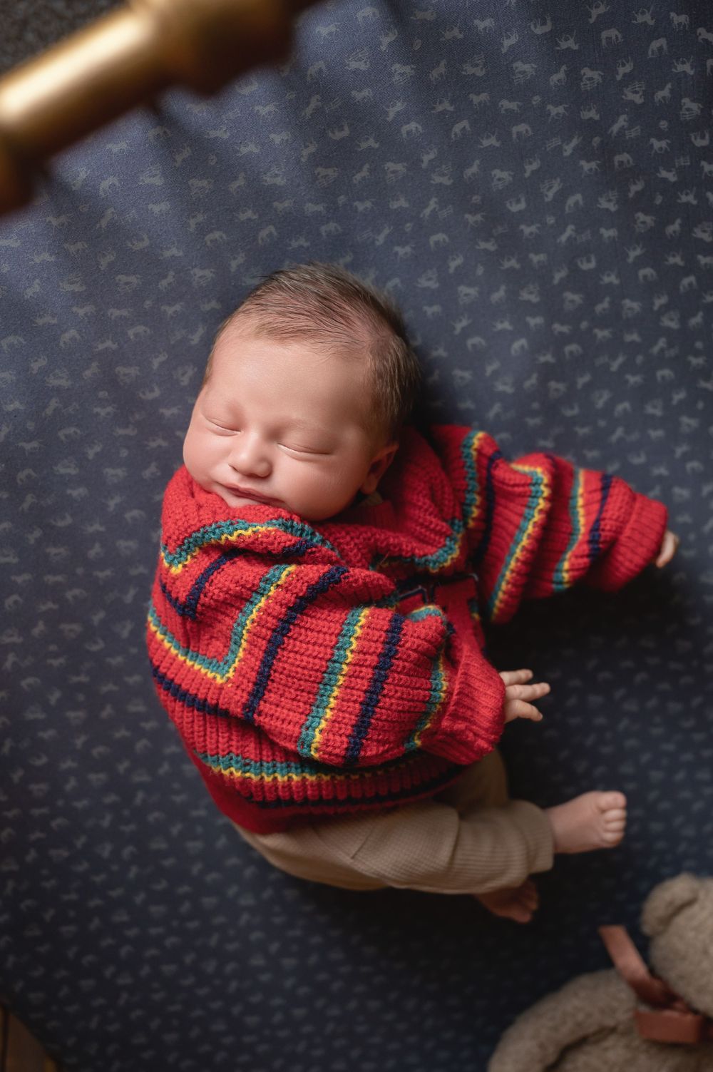 Sleeping newborn baby wearing a colorful red striped knit sweater, lying on a navy blue patterned blanket.