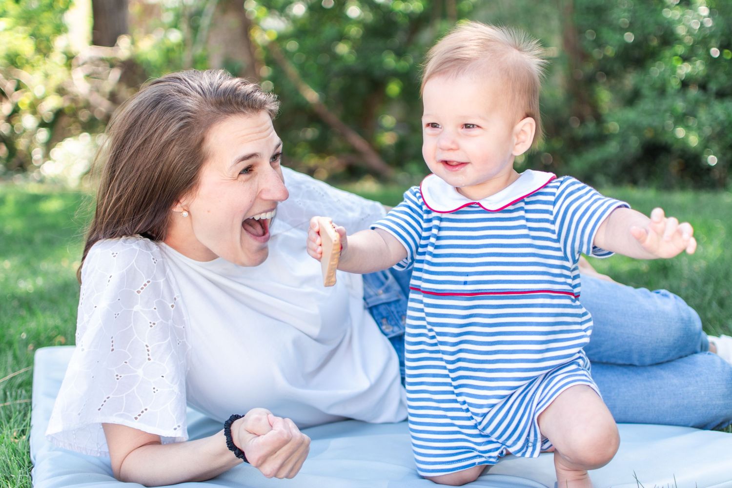 Woman and toddler playing and laughing together outdoors in a garden setting.