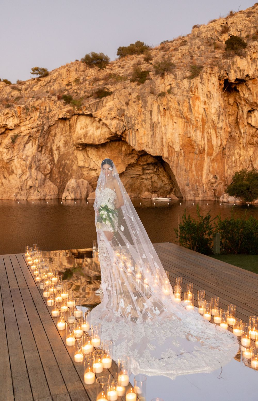 Wedding dress train surrounded by candlelight on wooden deck overlooking dramatic cliff face.