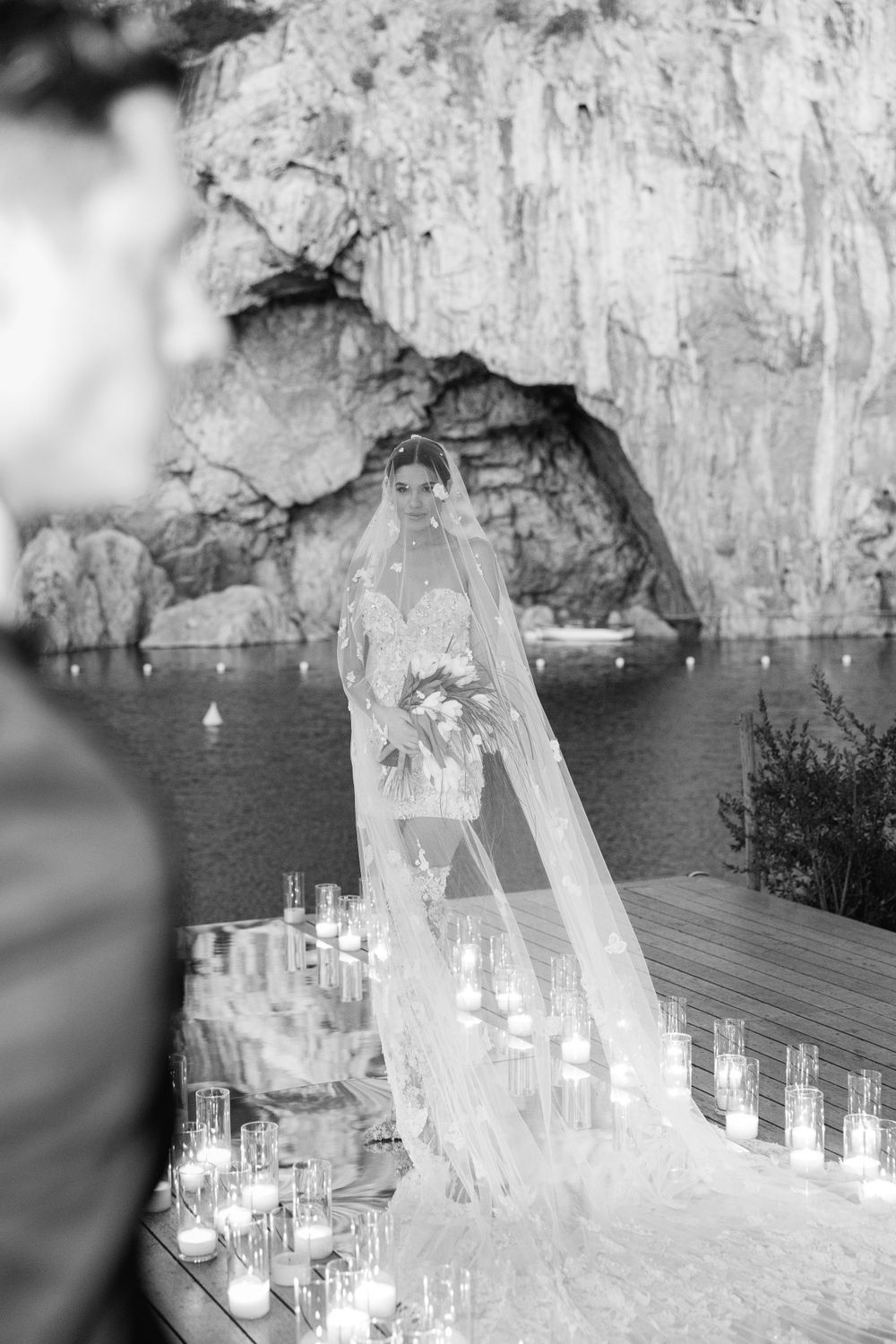 A flowing bridal veil drapes elegantly against a natural cave backdrop with glowing candles lining the ceremony space.