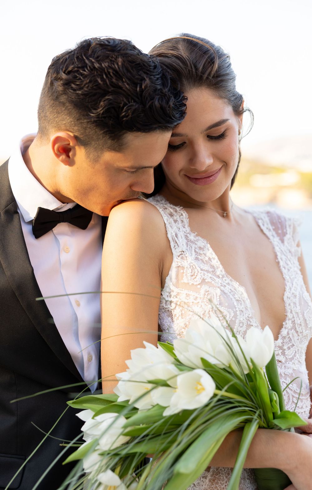 Romantic wedding couple embracing while holding white tulip bouquet against soft background.
