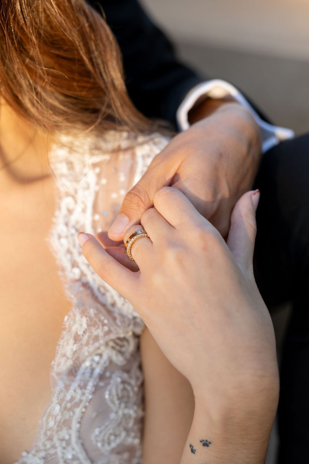 Close-up detail of delicate lace wedding dress and diamond ring with small wrist tattoo visible.