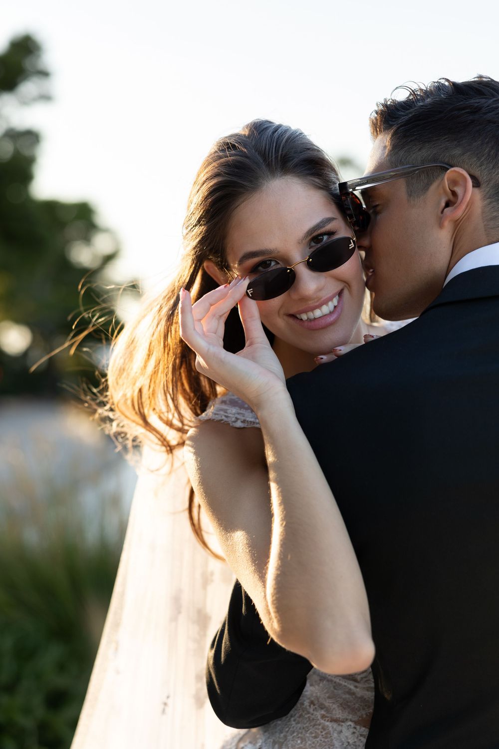 Intimate moment between newlyweds wearing sunglasses during outdoor sunset photoshoot.