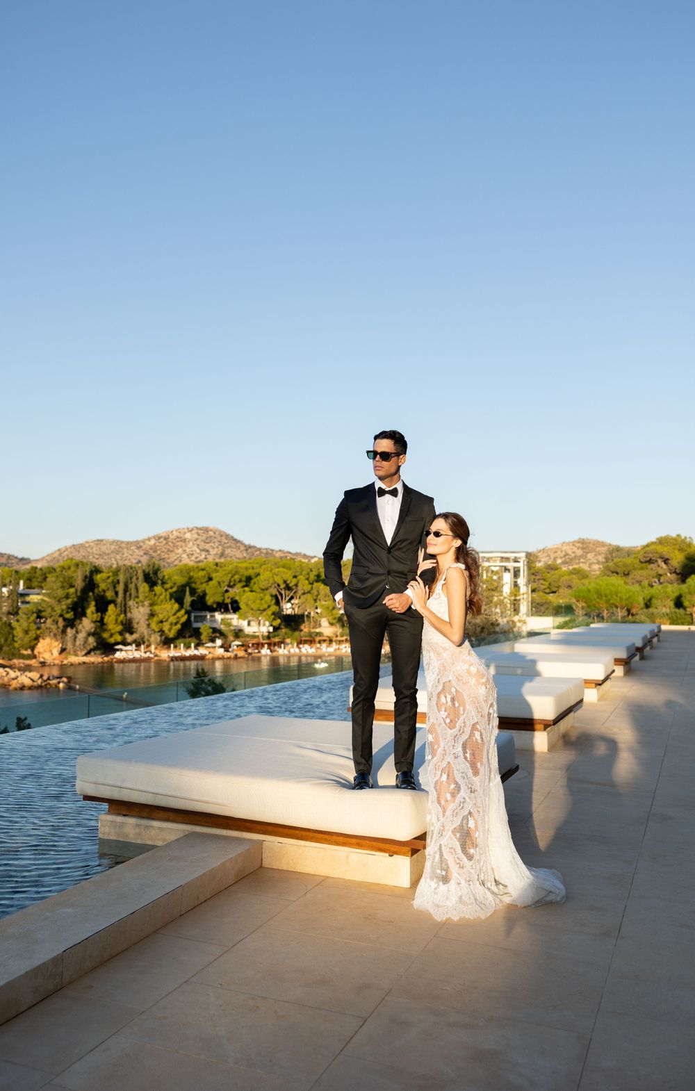 Newlyweds pose together on waterfront terrace with scenic mountain views during golden hour.