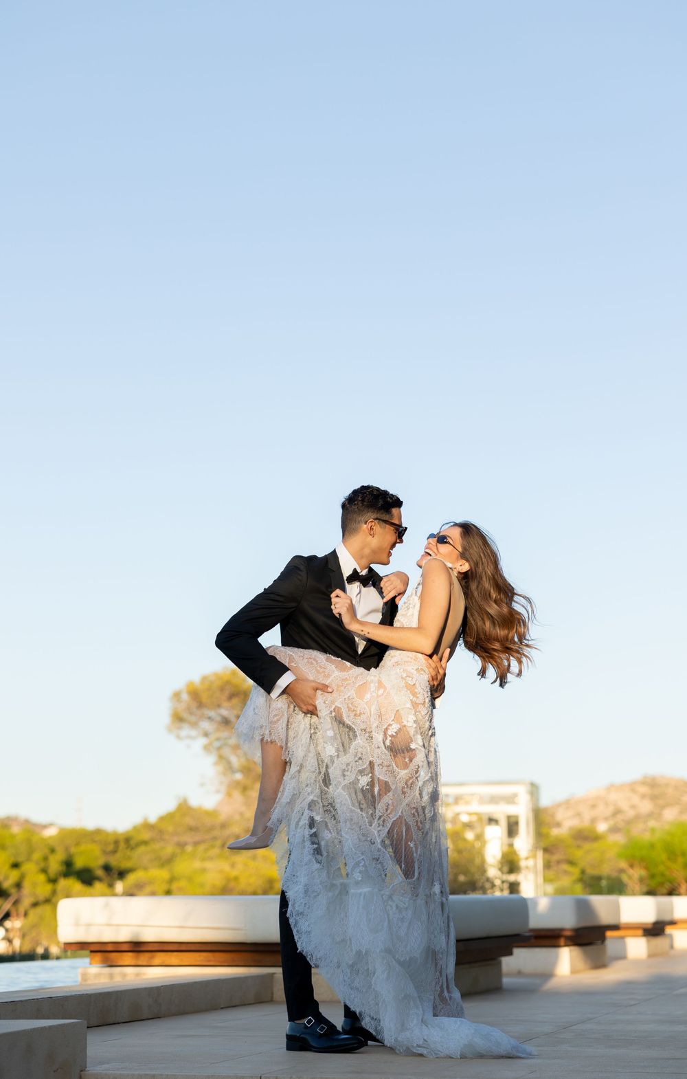 A romantic wedding photo of a couple dancing and embracing against a clear blue sky.