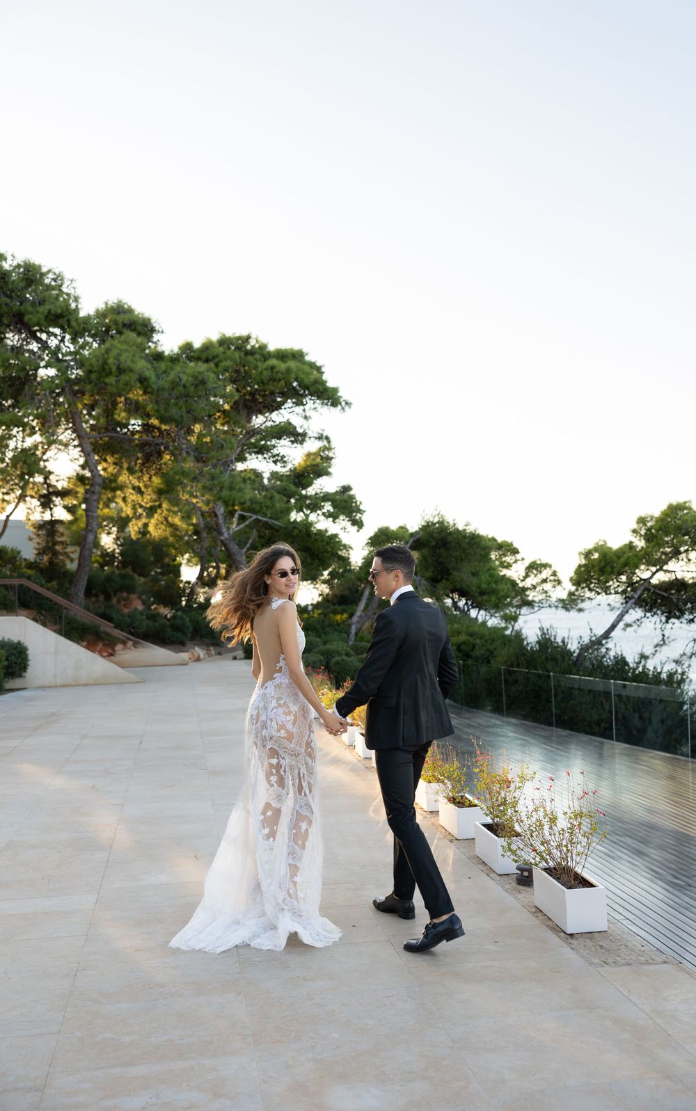 Couple in wedding attire walking on outdoor terrace during golden hour.