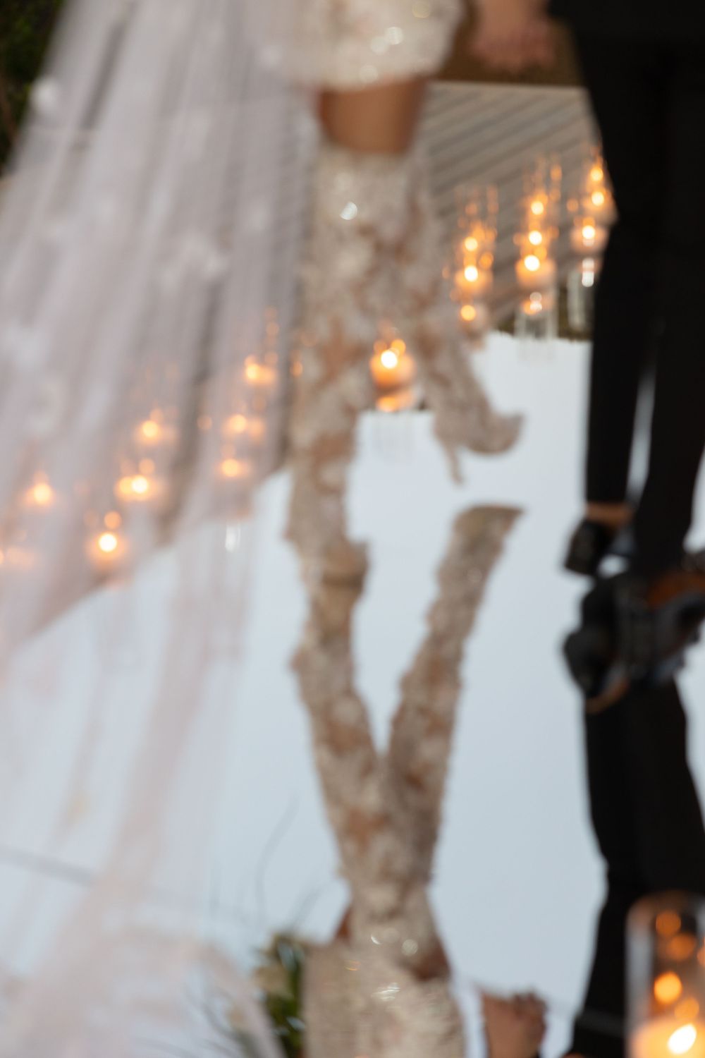 Blurred detail shot of lace wedding dress with candlelit accents in background.