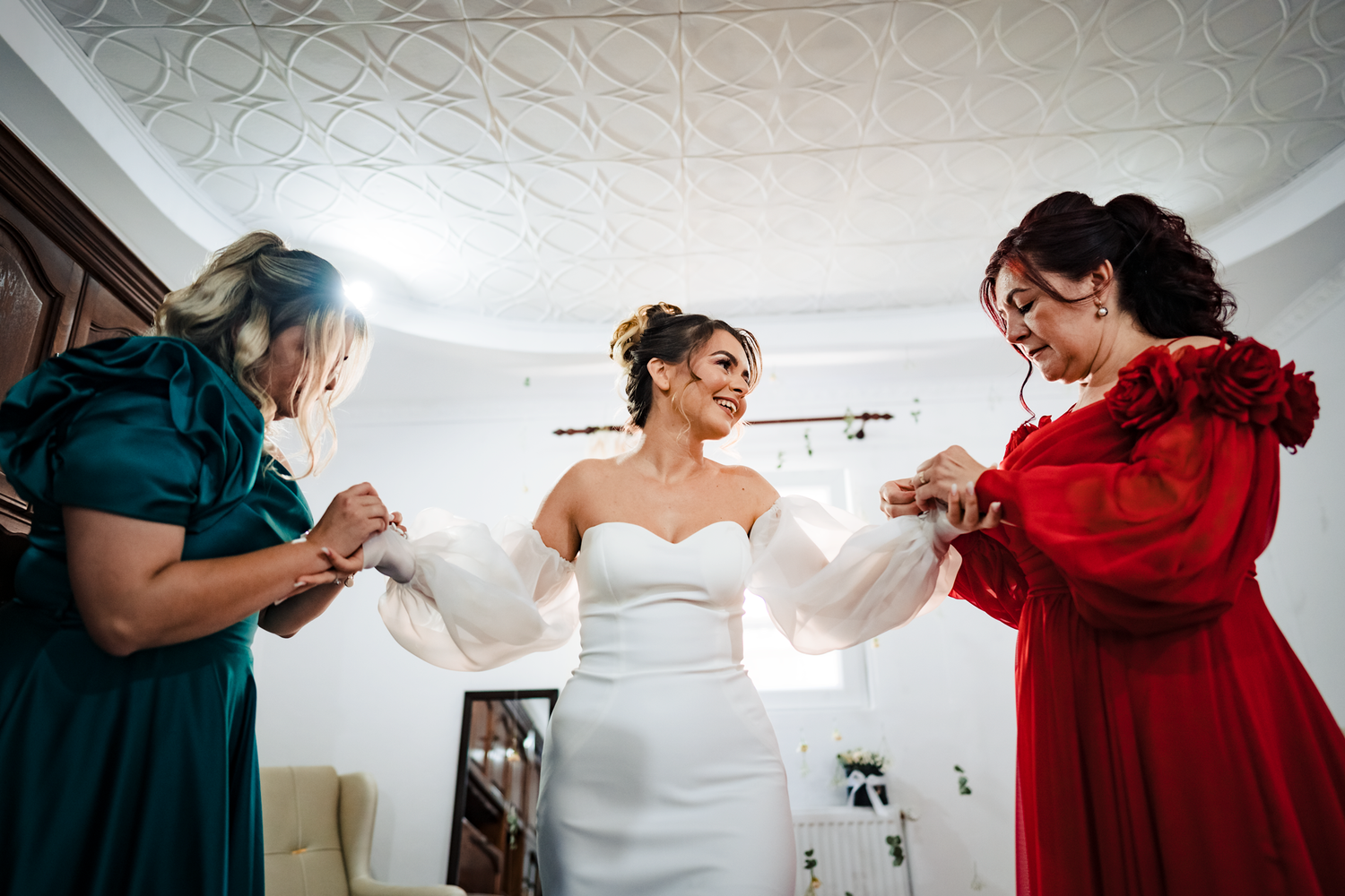 Getting ready sequence showing bridesmaids helping bride with wedding dress preparations.