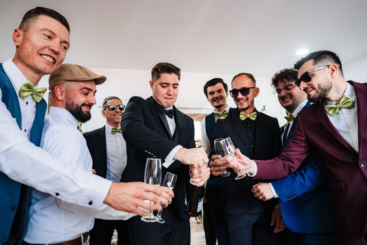 Groomsmen in formal attire sharing drinks and laughter during wedding preparations.