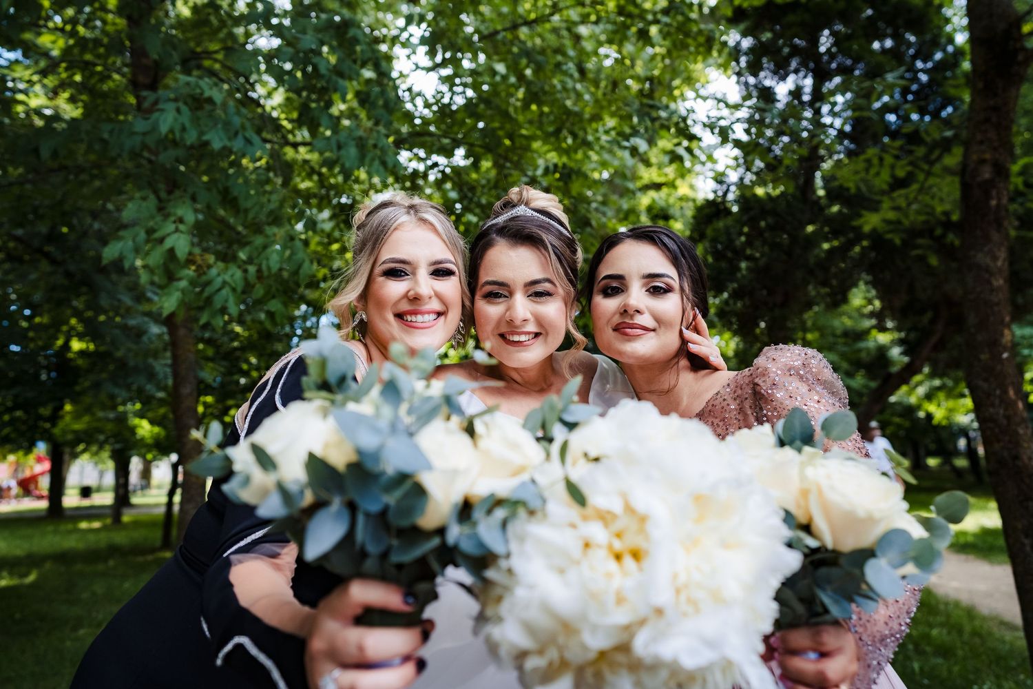 Wedding party members hold white floral bouquets while posing in garden setting.