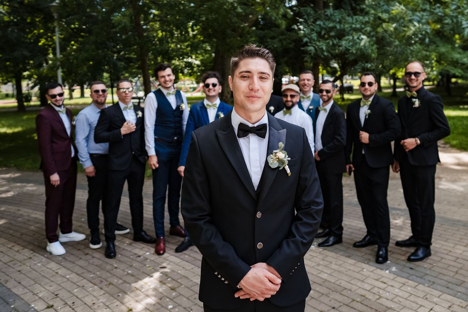 Large wedding party gathers outdoors for formal group photos on brick pathway.