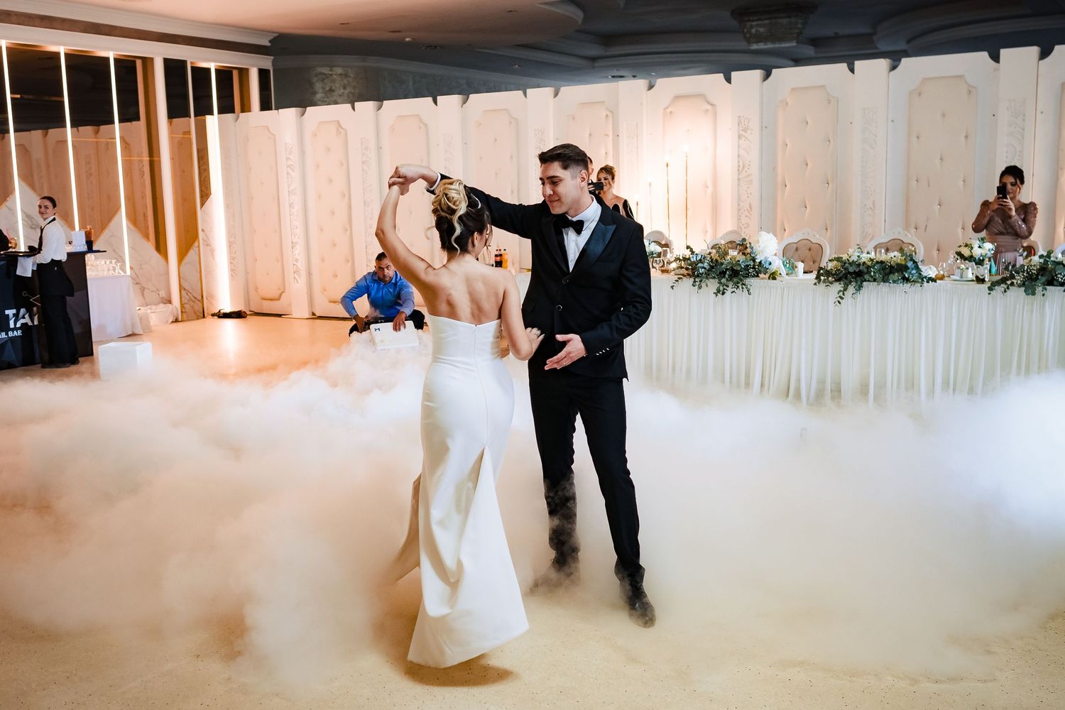 Dancers glide across a pristine white ballroom during an elegant celebration.