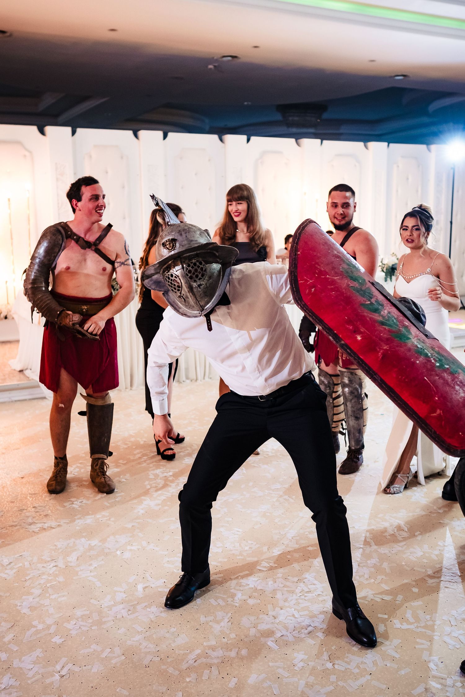 Performers dressed as gladiators with shields pose dramatically at themed wedding celebration.