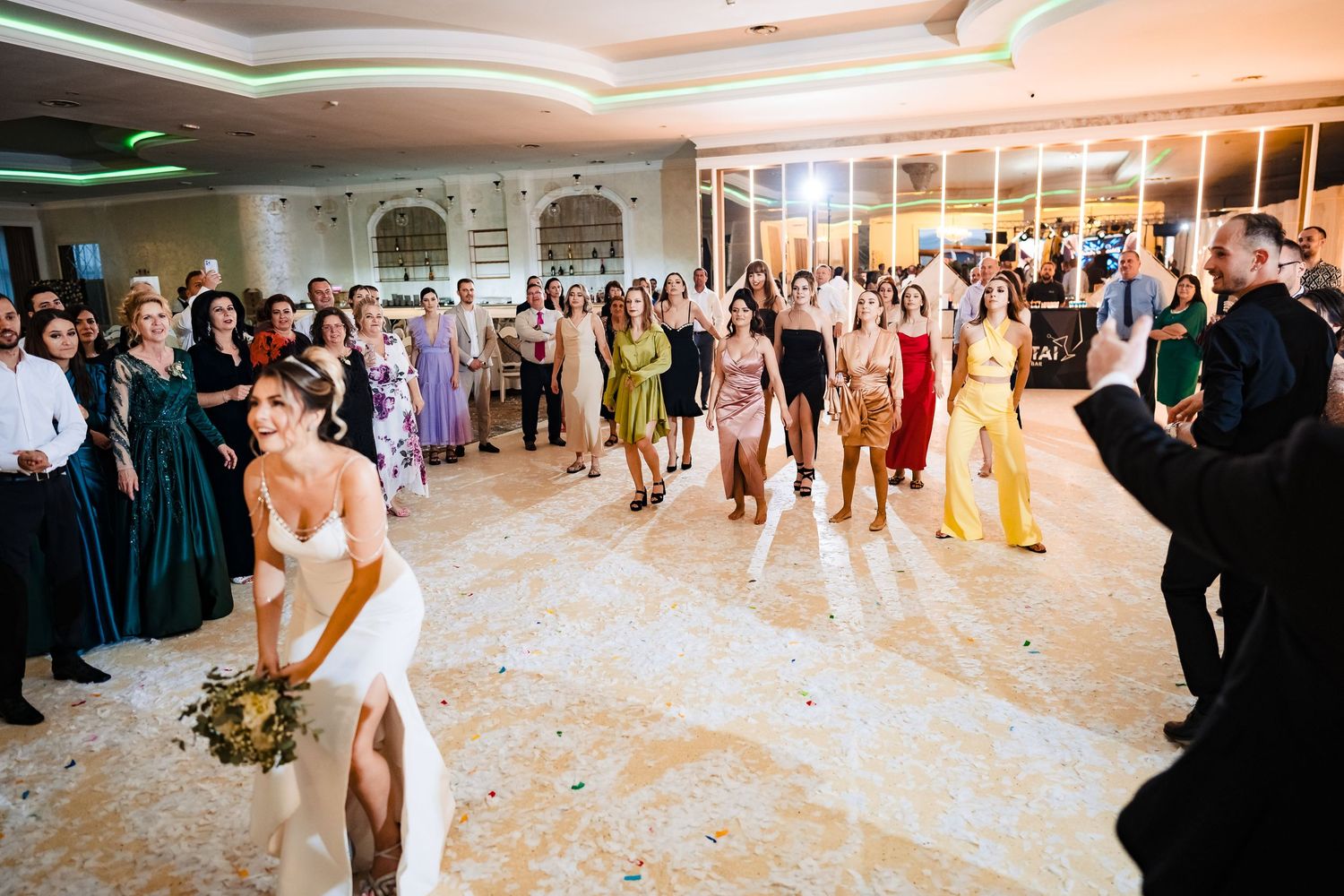 Wedding guests gather in an elegant ballroom as someone prepares to toss a bouquet during a reception celebration.