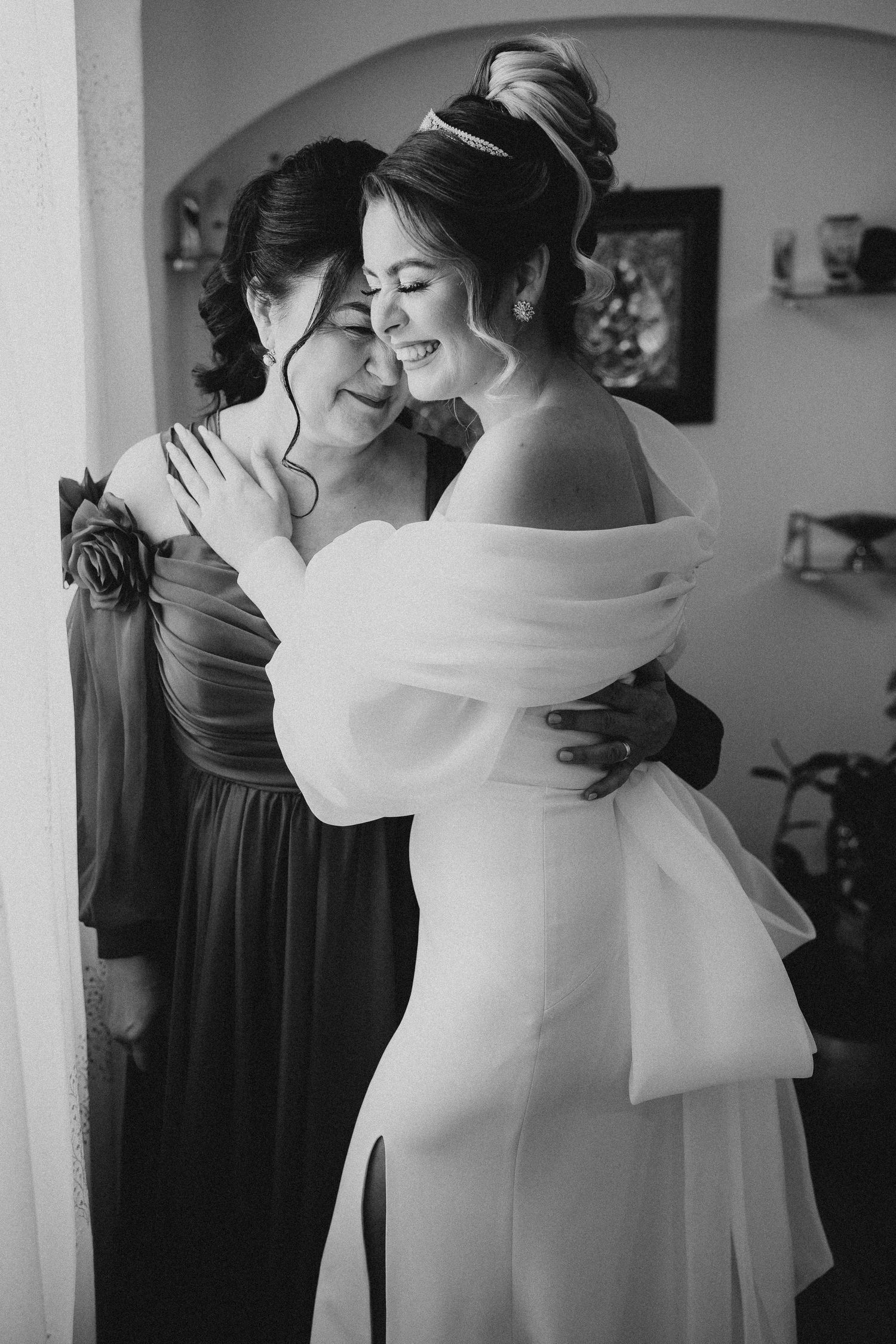 Black and white emotional wedding moment showing embraces between bride and bridesmaids in formal dresses.