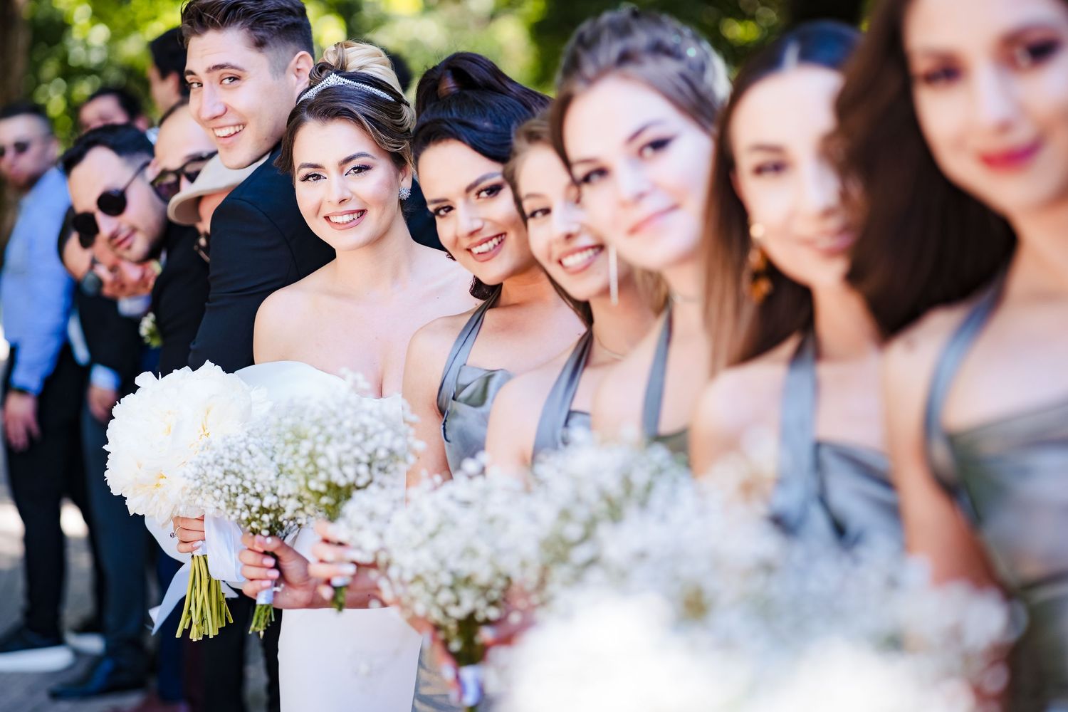 Bridesmaids holding white floral bouquets smile together in a group photo.