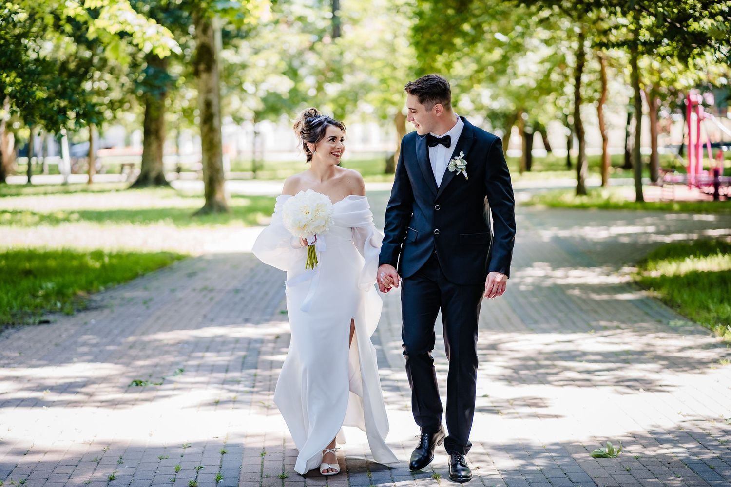 A wedding couple walks together on a tree-lined path on their special day.