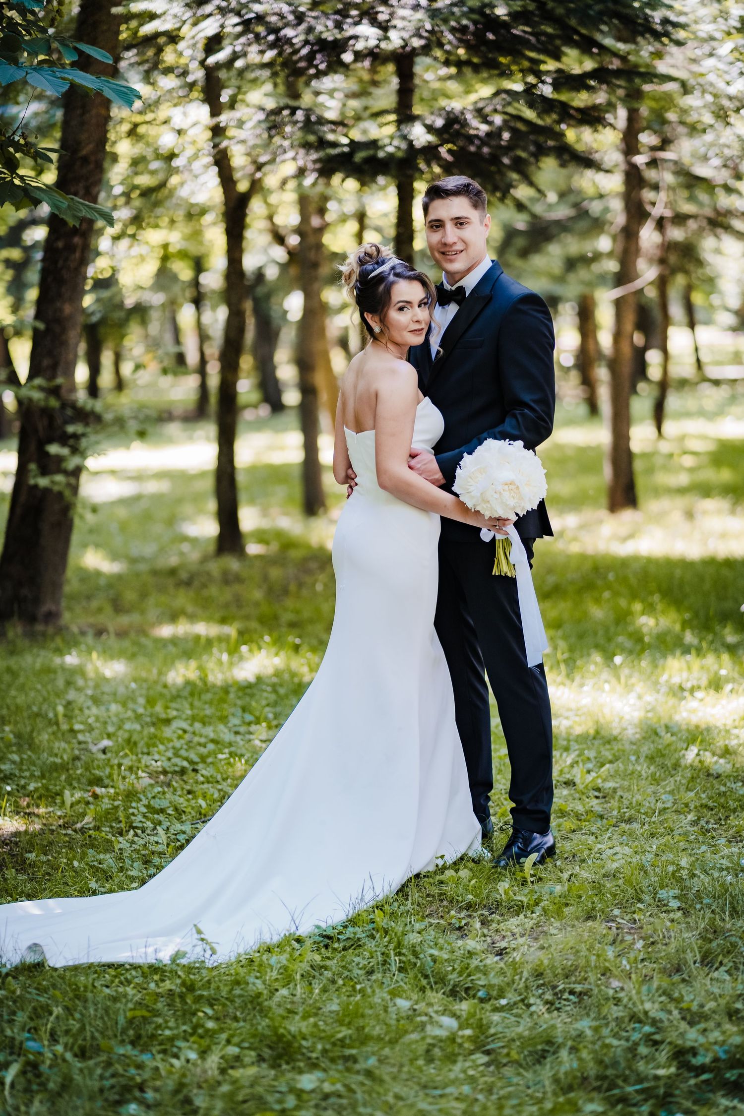 Couple dancing together in a scenic outdoor forest setting with sunlight filtering through the trees.