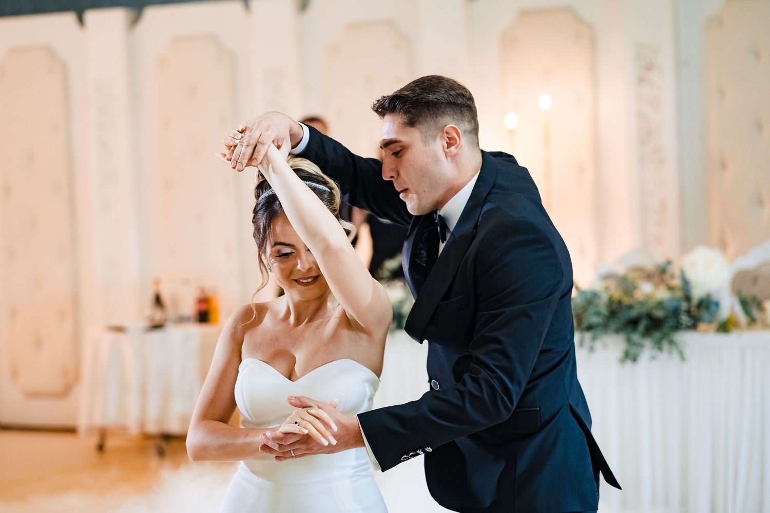 Newlyweds share their first dance in an elegant ballroom with romantic lighting and floral decorations.