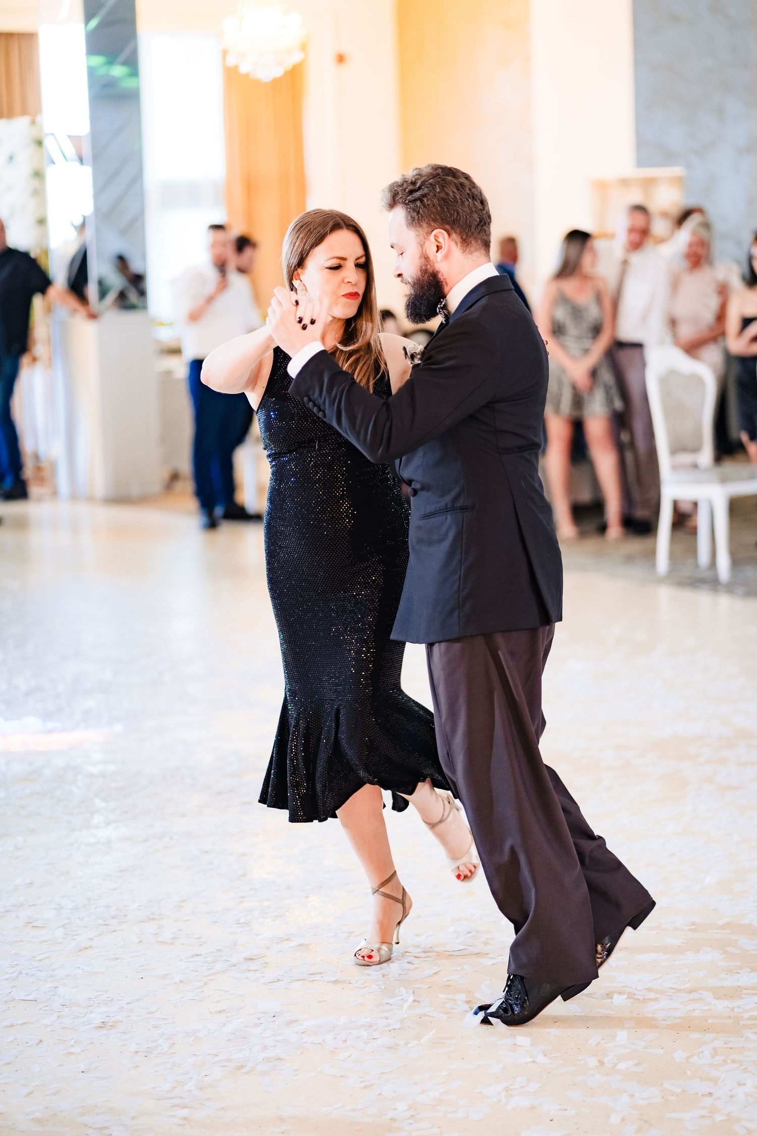 A couple performs an elegant ballroom dance move in formal attire on a polished dance floor.