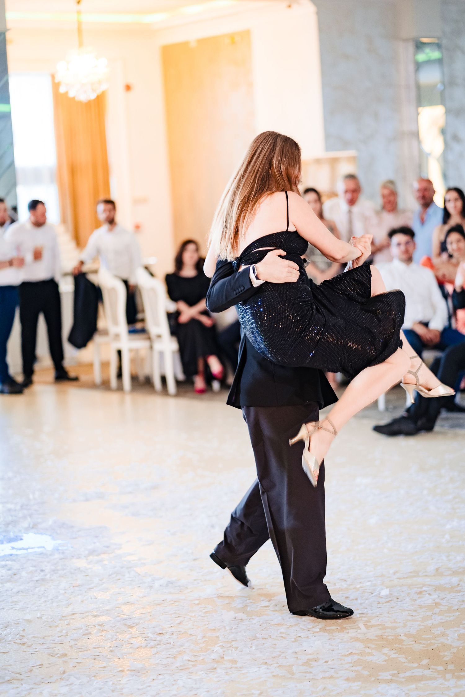Dancers execute a dramatic dip move during a ballroom performance in formal black attire.