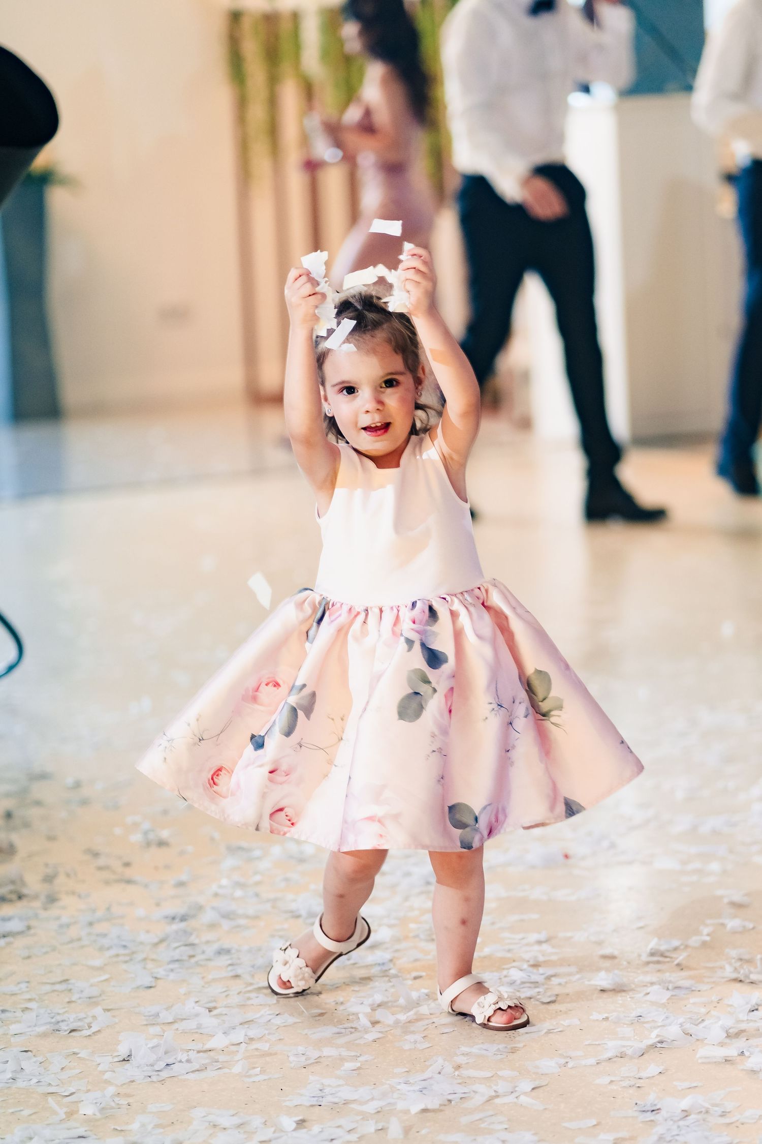 Young child in pink floral dress dances joyfully at wedding reception.
