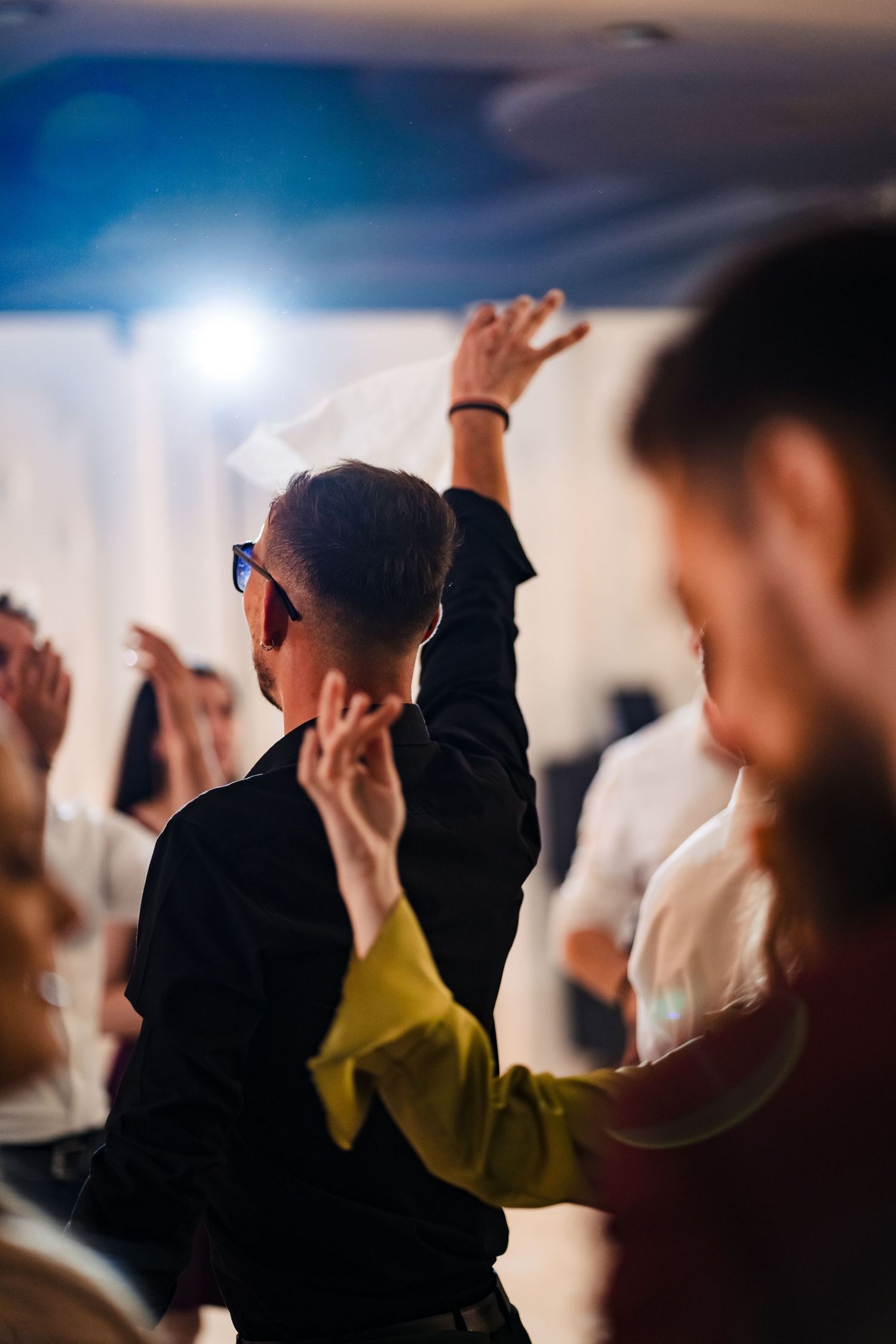 Party guests dance with raised arms under dramatic blue lighting at a celebration event.