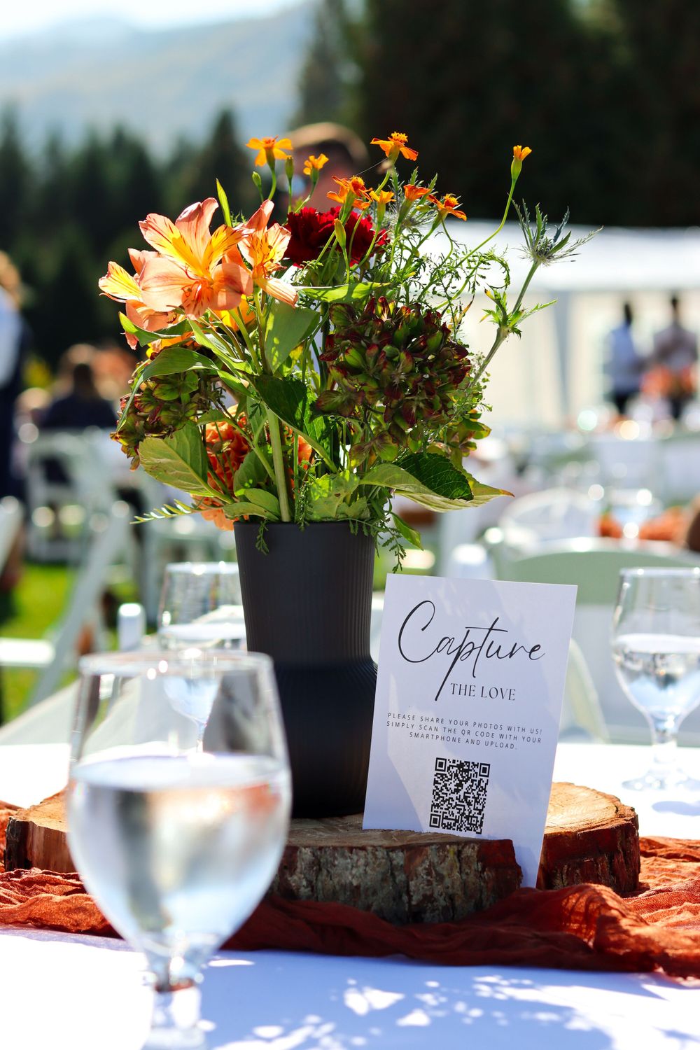 Outdoor wedding table centerpiece with orange flowers and a QR code card.