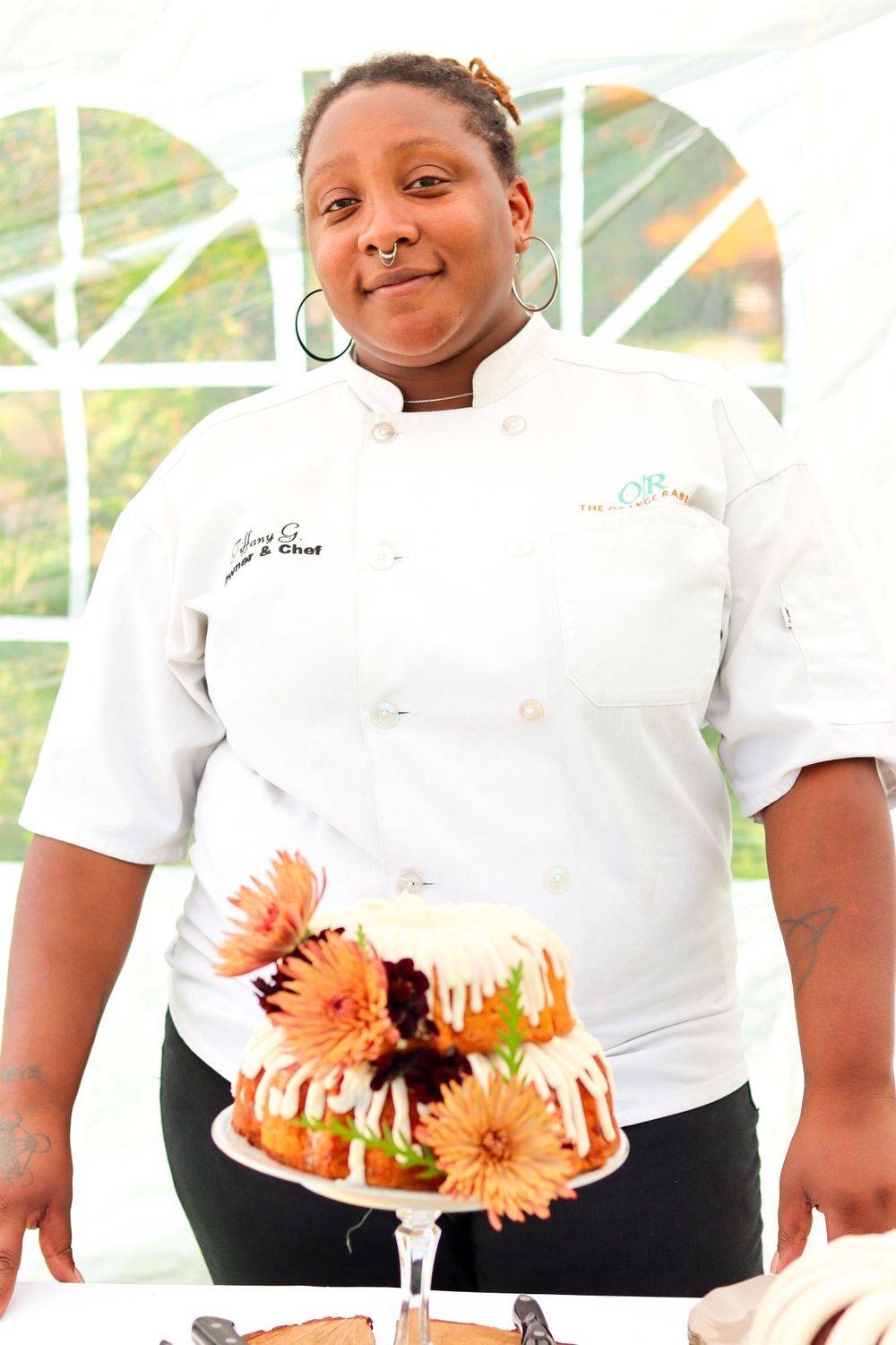 Professional chef in white uniform showcasing a beautifully decorated dessert with fresh flowers.