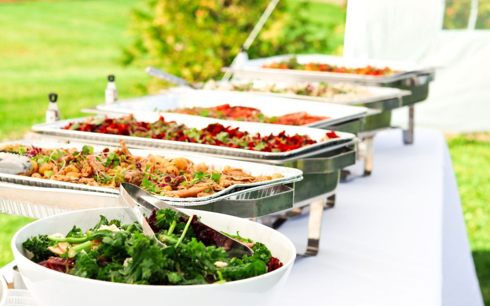 Elegant catering buffet setup with chafing dishes and fresh salad at an outdoor event.