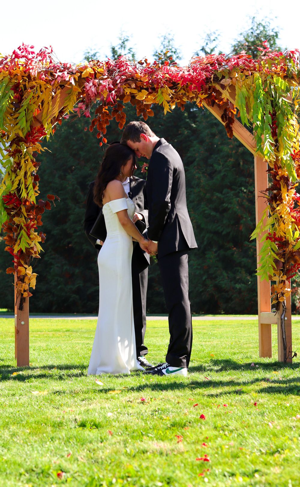 Couple sharing intimate moment under floral arch with vibrant fall foliage.