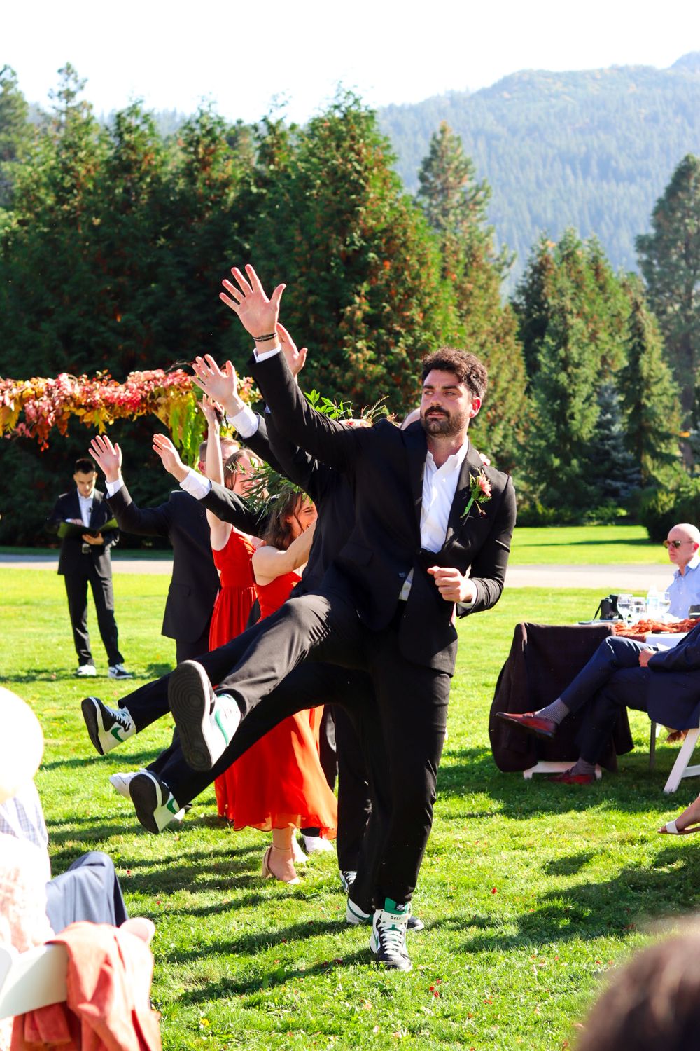 Wedding guests dancing and celebrating on a lawn with mountains in the background.