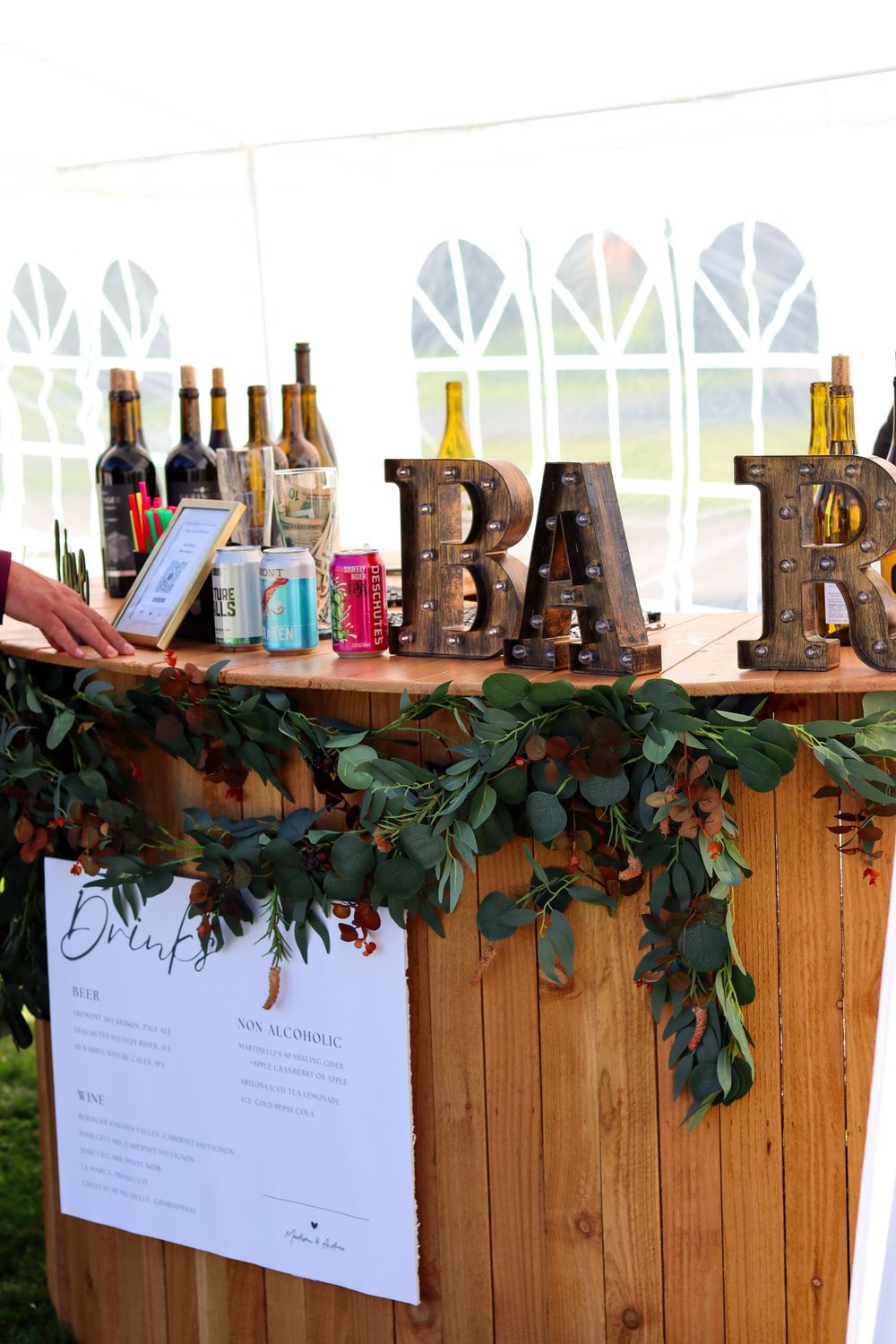 Rustic wooden bar setup with decorative BAR letters and greenery garland.