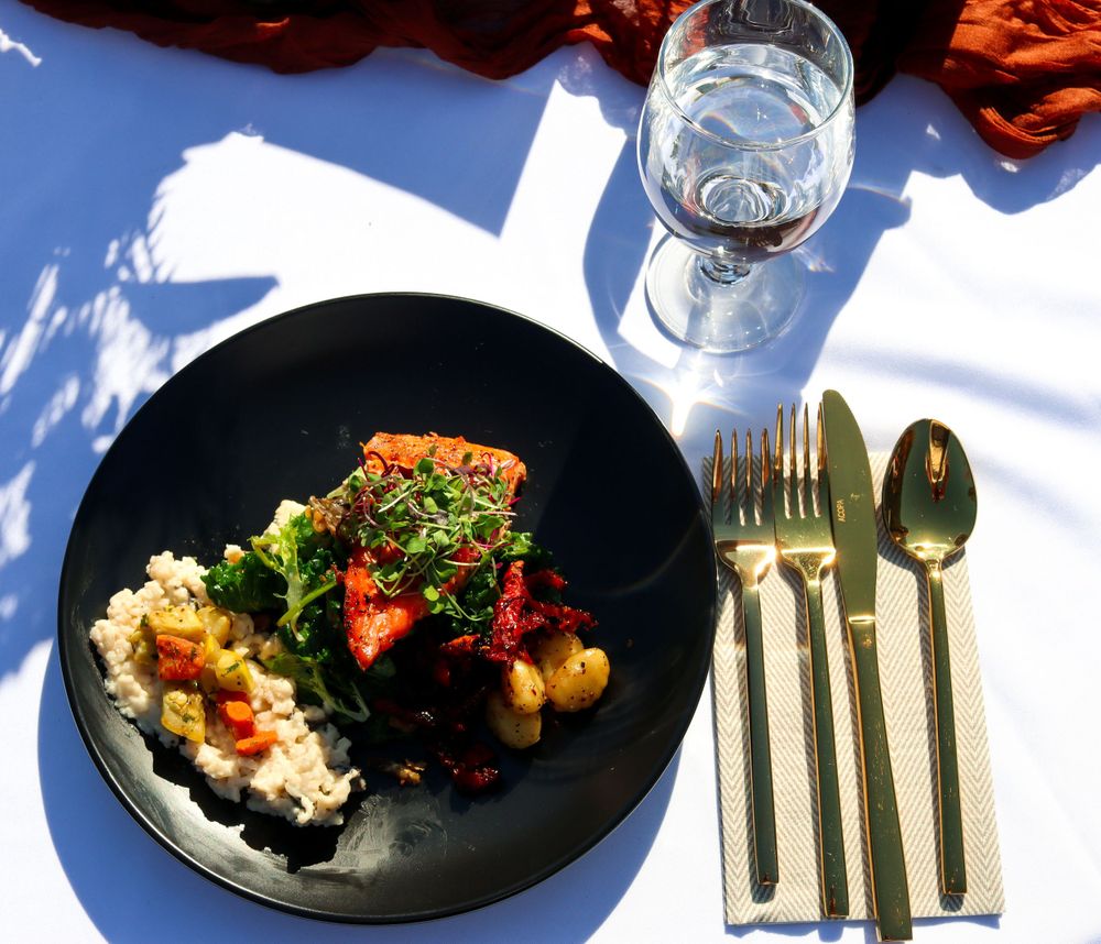 Gourmet plated dish with rice and vegetables served with gold cutlery on black plate.