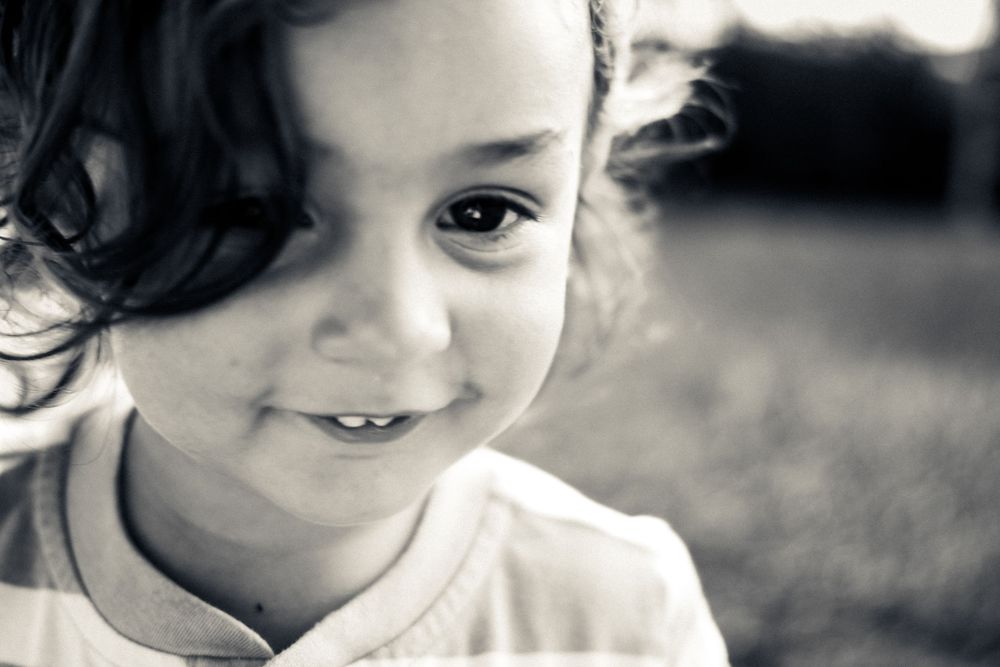 Black and white portrait photograph showing a close up shot of a child's joyful expression and dark hair outdoors.