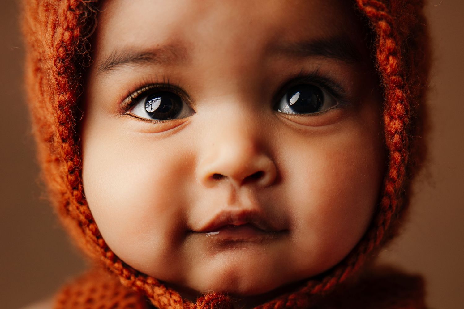 Close-up profile of child wearing orange knit bonnet against warm brown background.