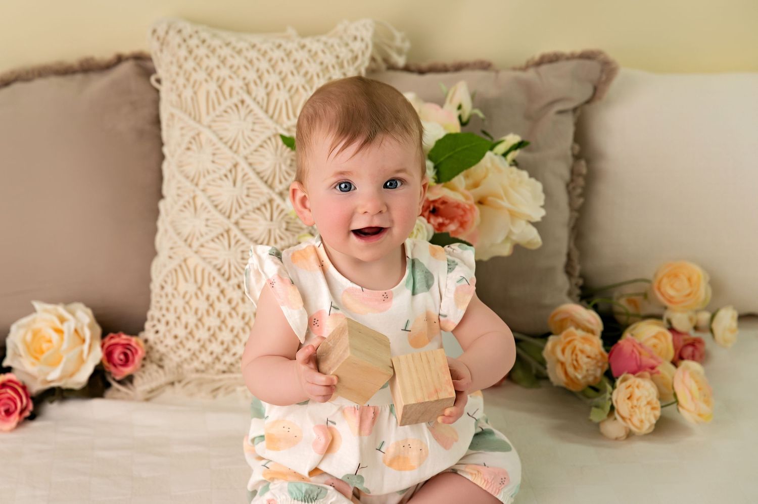 Joyful baby wearing white sweater lies on soft gray blanket with bright smile and sparkling eyes.