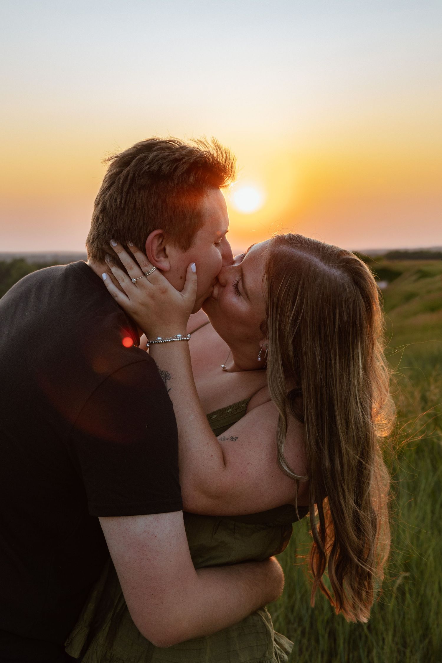 Couple sharing a romantic kiss in a green field during a golden sunset.