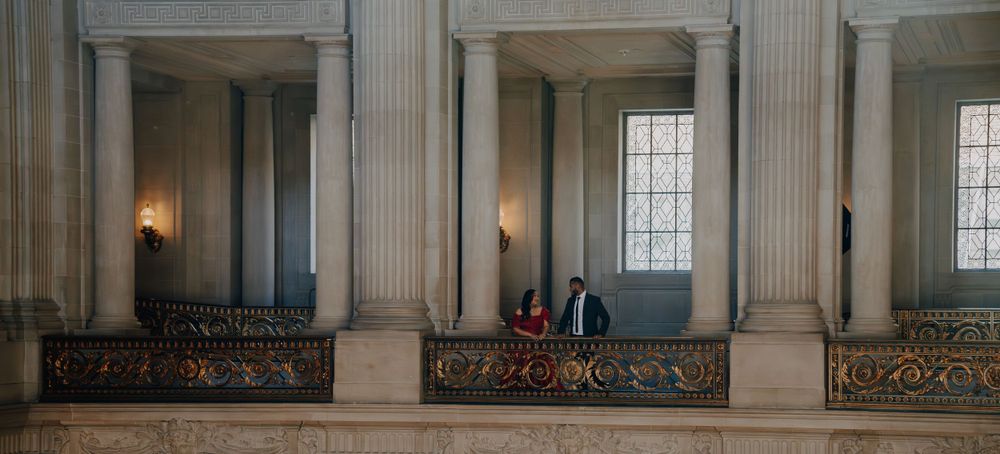 A couple stands in candlelit alcoves with ornate architectural details and iron railings.