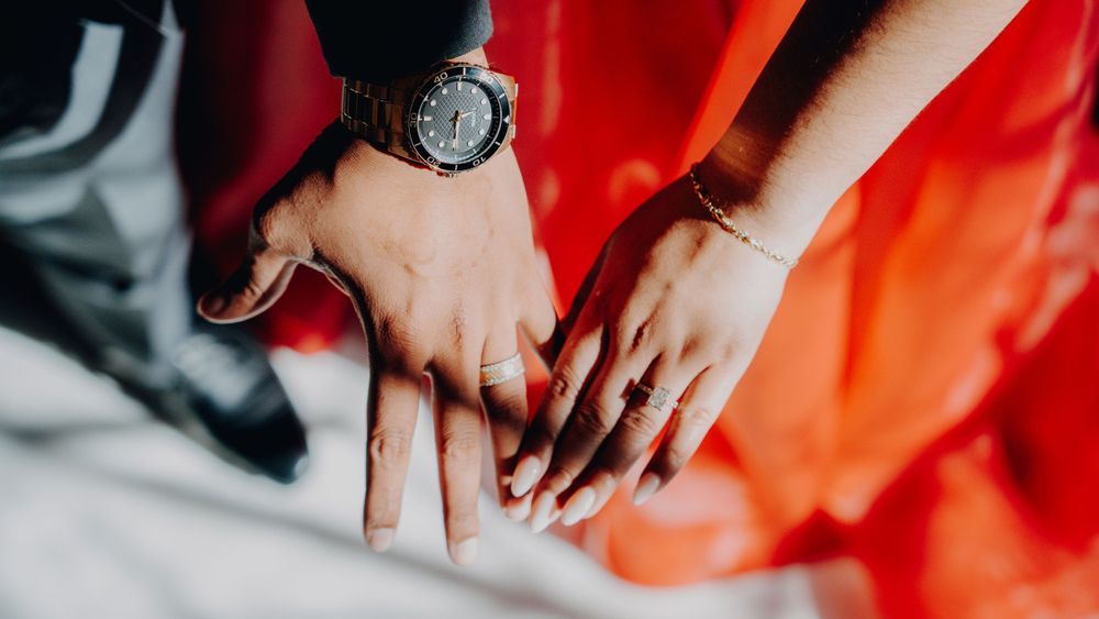 Close-up of hands with engagement ring against red fabric and formal attire.