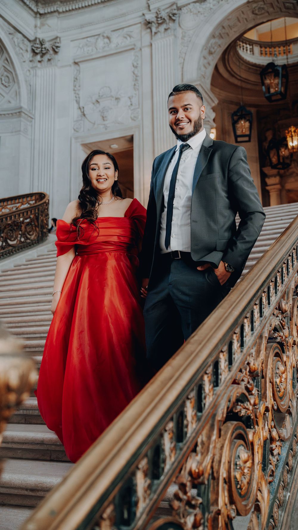 Couple in formal wear standing on an elegant staircase with ornate architectural details.