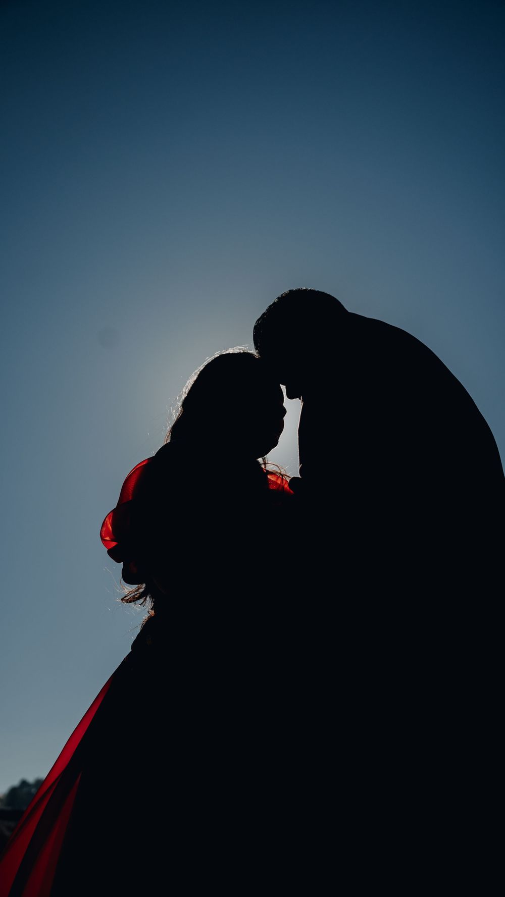 Silhouette of a couple against blue sky with flowing red dress creating dramatic contrast.