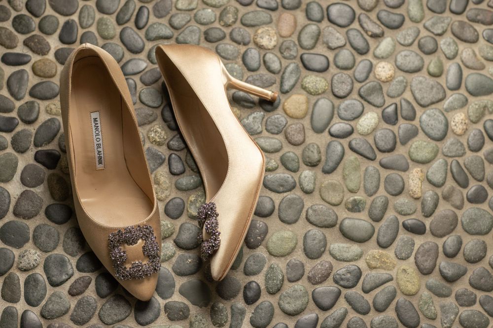 Elegant Manolo Blahnik bridal heels with jeweled buckle detail on a pebble stone floor.